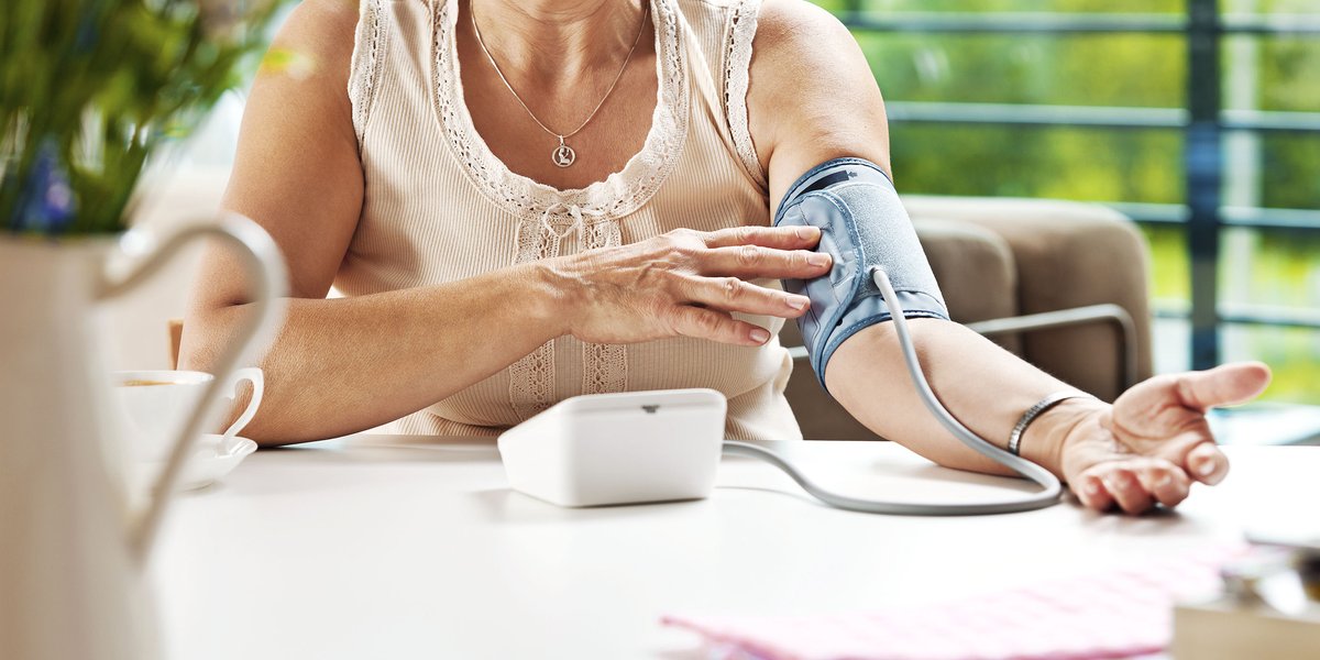 Woman sitting at a table using a blood pressure reader to measure her own blood pressure