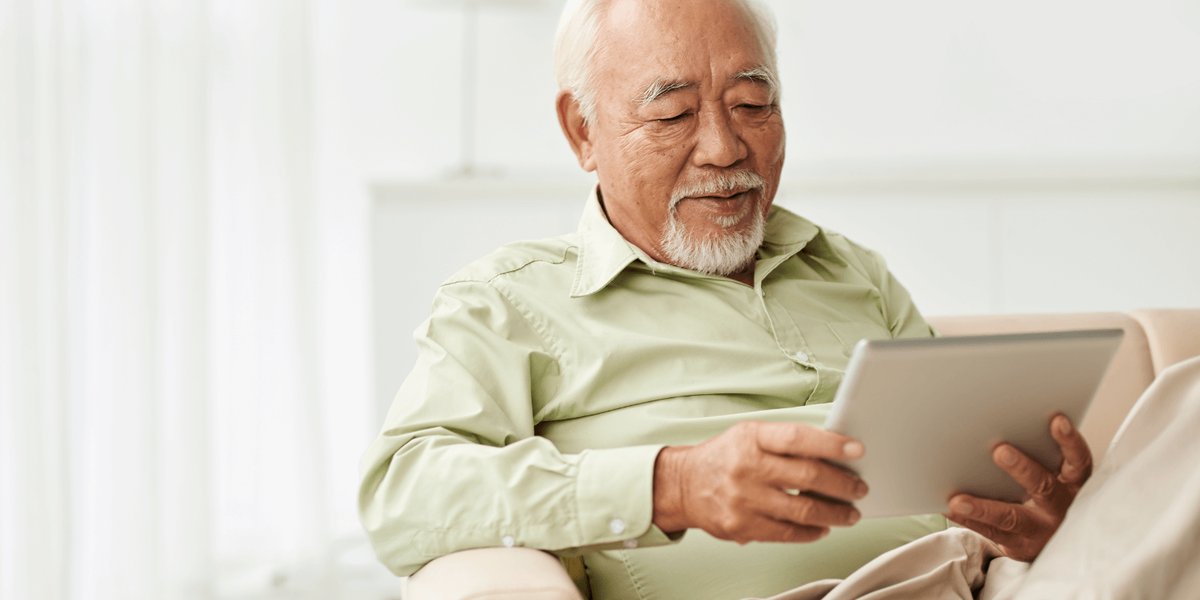 Elderly man sitting on a couch with his tablet device.