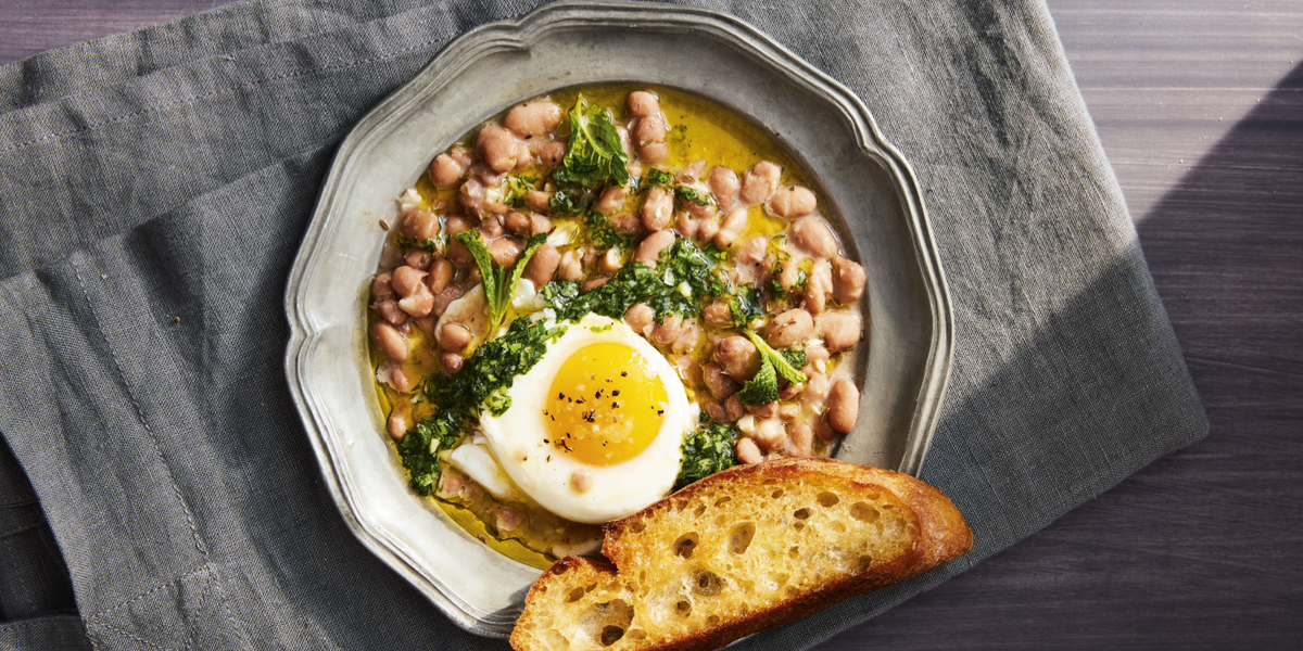 bowl of saucy beans and eggs with a piece of bread on a table