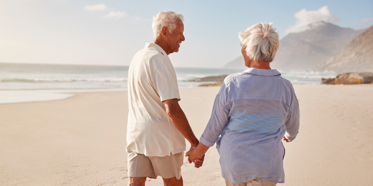 Elderly couple smiling and holding hands while walking on an empty beach.