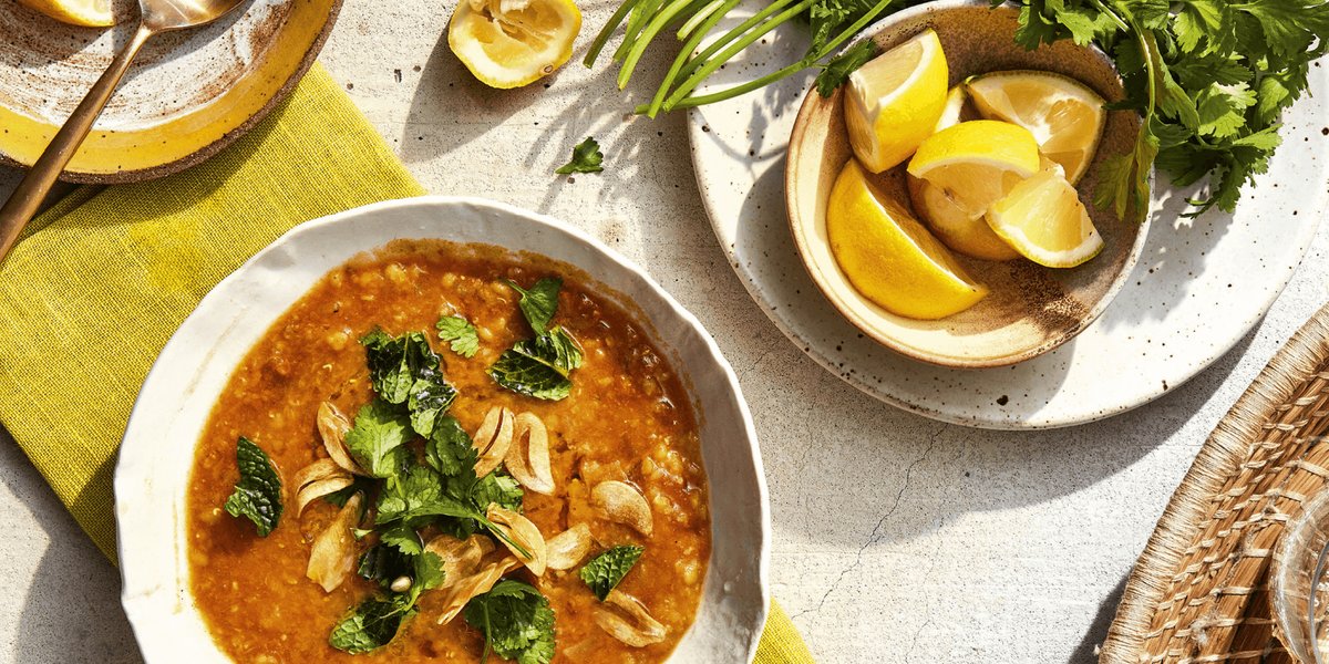bowl of red lentil dal with lemons and herbs on a table