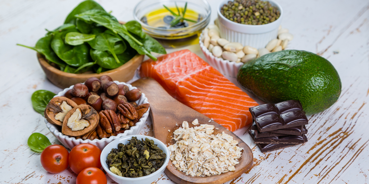 Variety of nutritional food such as salmon, avocado, spinach tomatoes, and grains on a table.