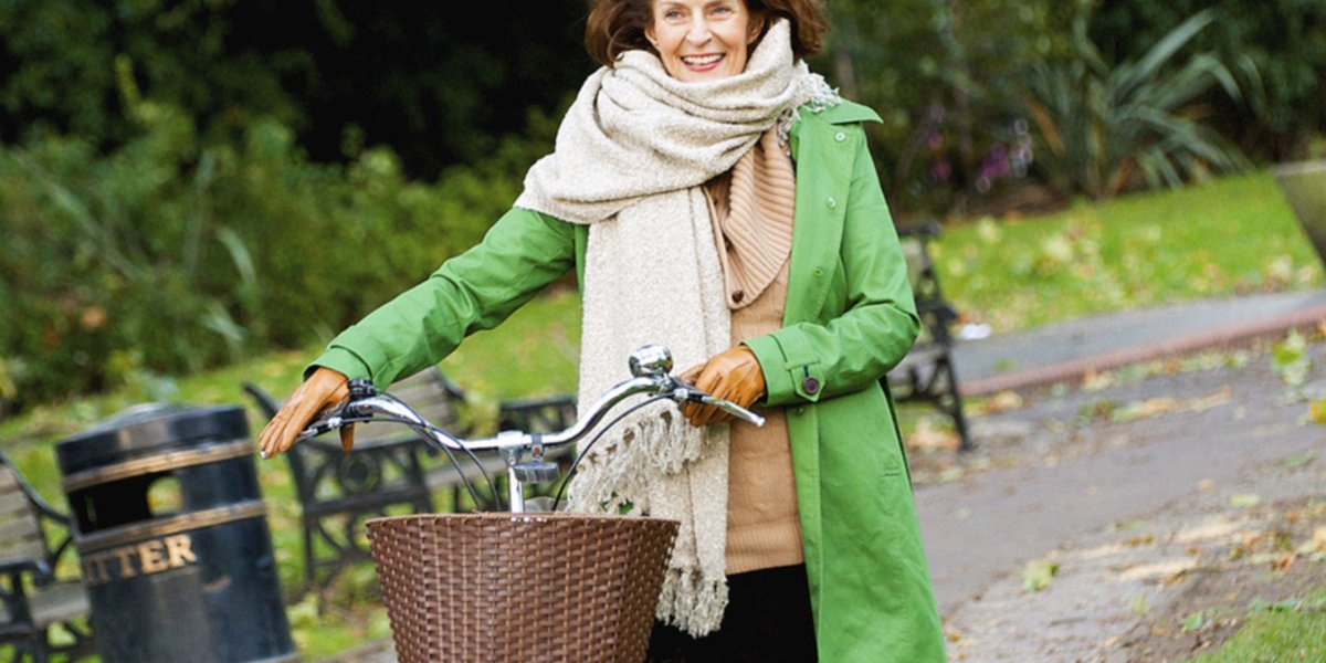 Woman in a green jacket walking her bicycle outside