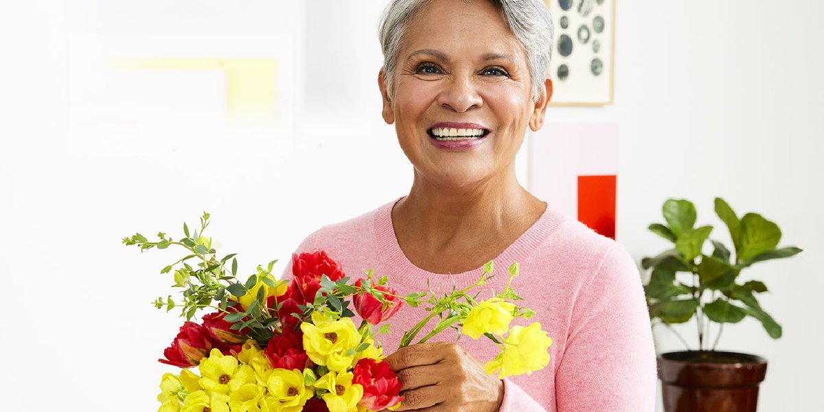woman in a pink sweater arranging a bouquet of yellow, red, and pink flowers on the countertop in the kitchen