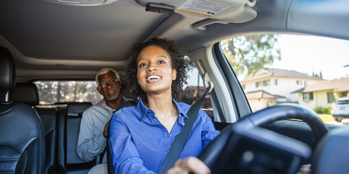 Young woman in a car driving with an elderly man in the back seat.