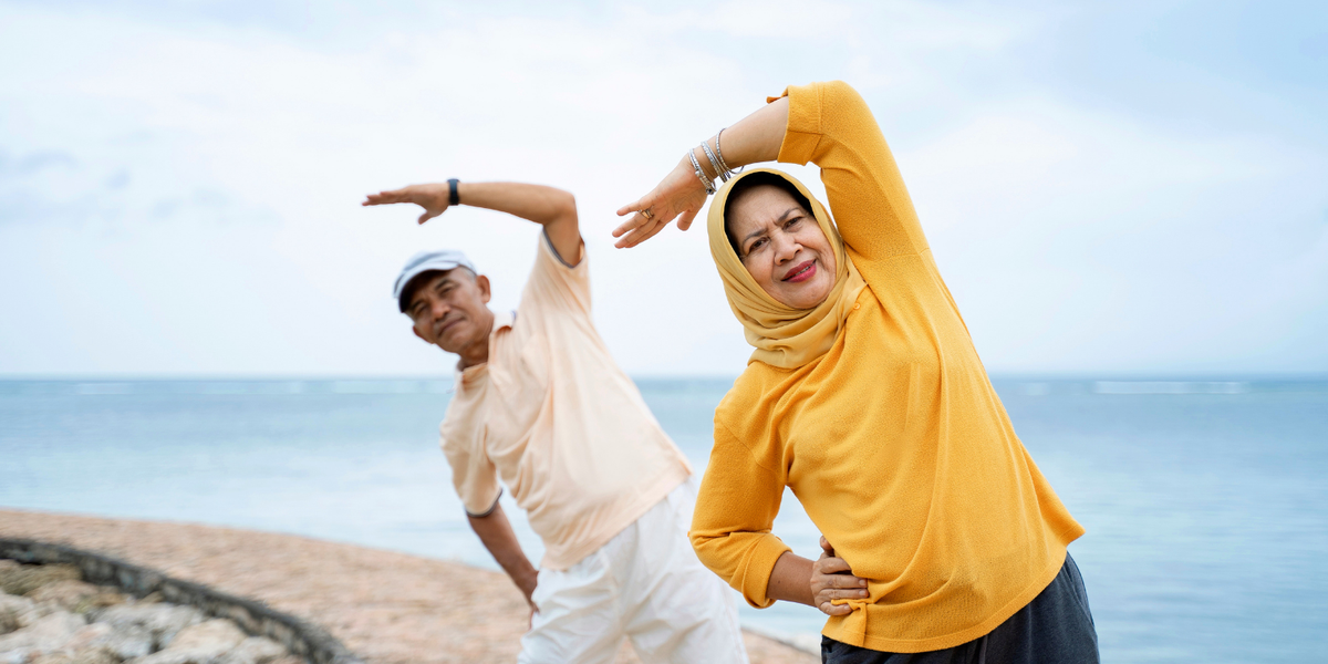 Woman in a yellow shirt and yellow headscarf with a man in a white polo stretching by the water