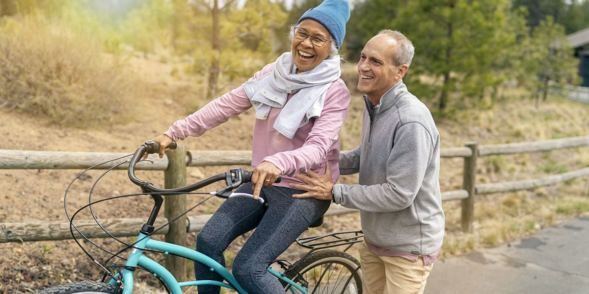 Woman on a blue bicycle with a man helping her learn how to ride the bicycle