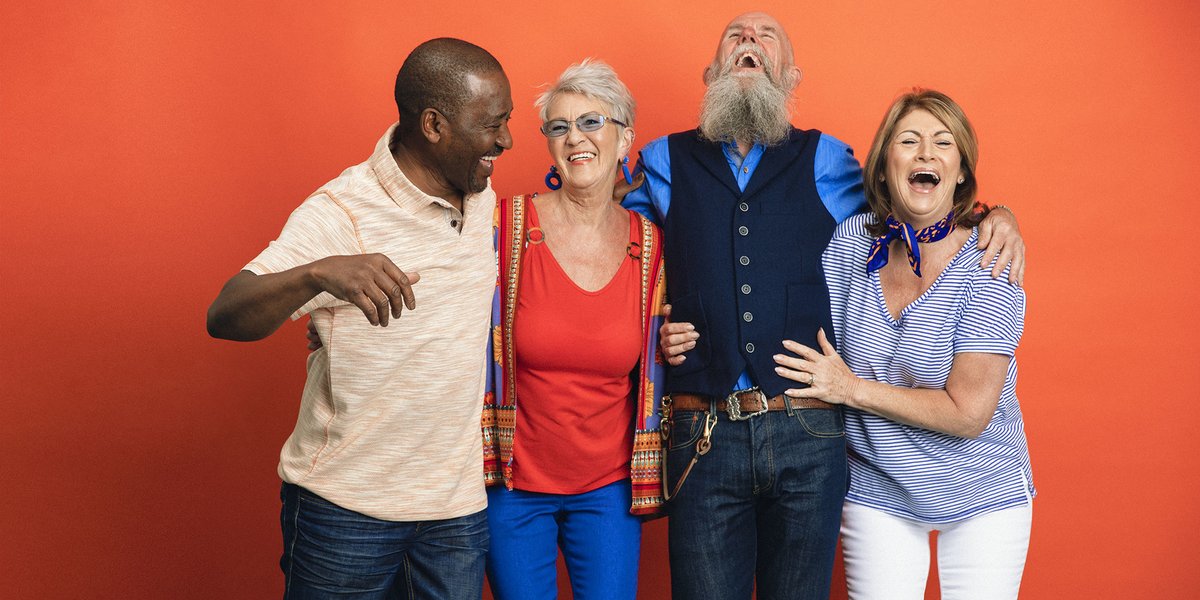 Group of 4 friends laughing with each other in front of an orange wall
