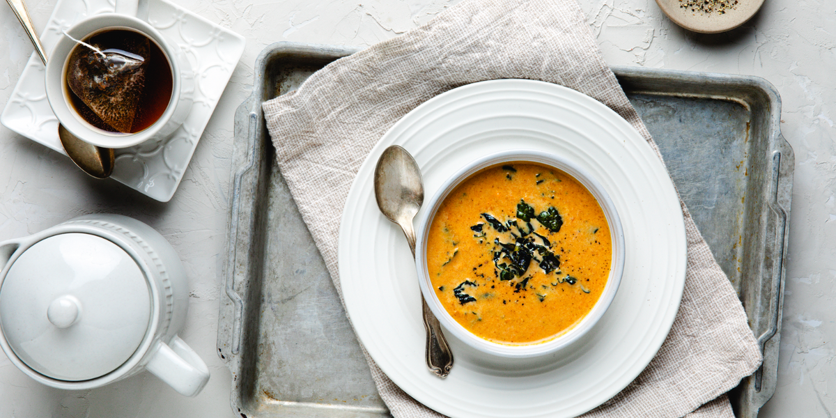 A bowl of sweet potato soup on a concrete table with a teapot and tea cup next to it.