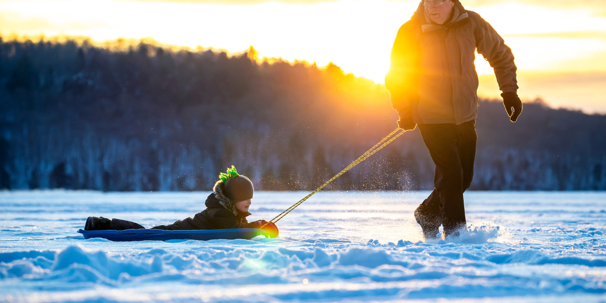 Grandfather pulling grandson on a sled on a snowy day.